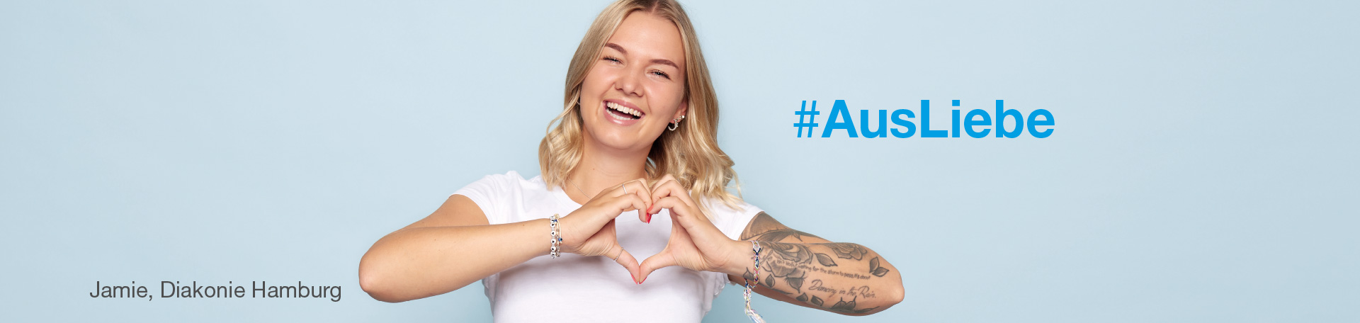 #AusLiebe - Frau mit Tattoo formt mit Händen Herzsymbol